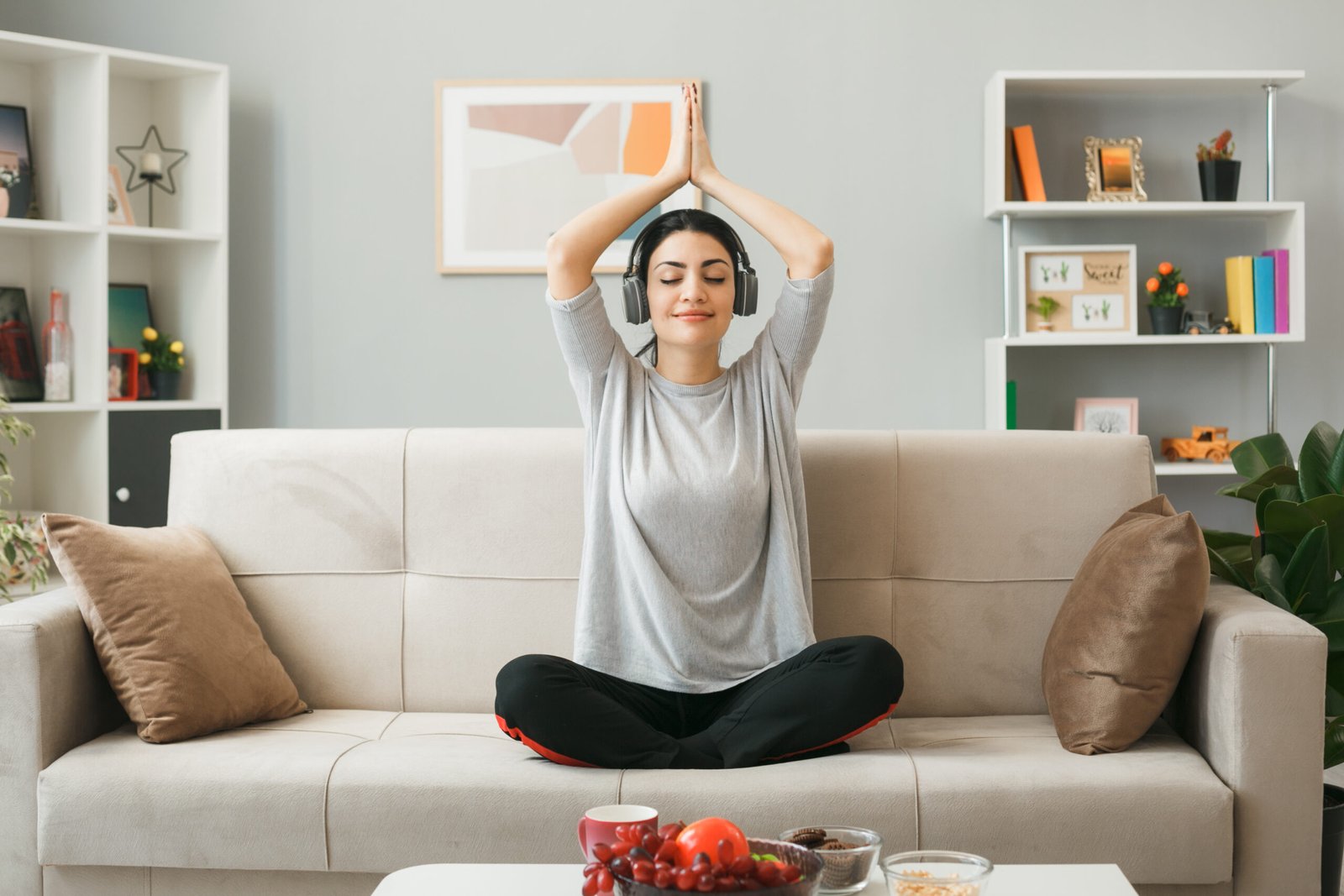 pleased-young-girl-wearing-headphones-doing-yoga-sitting-sofa-coffee-table-living-room